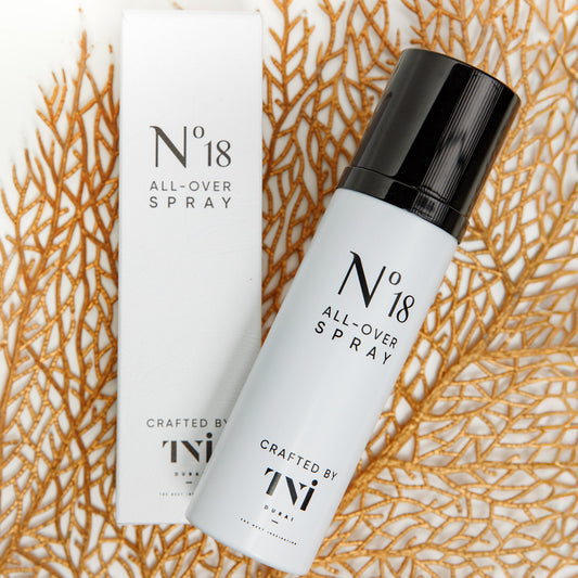A white bottle with black cap labeled 'N°18 ALL-OVER SPRAY' placed on a surface with a decorative golden coral-like texture in the background.